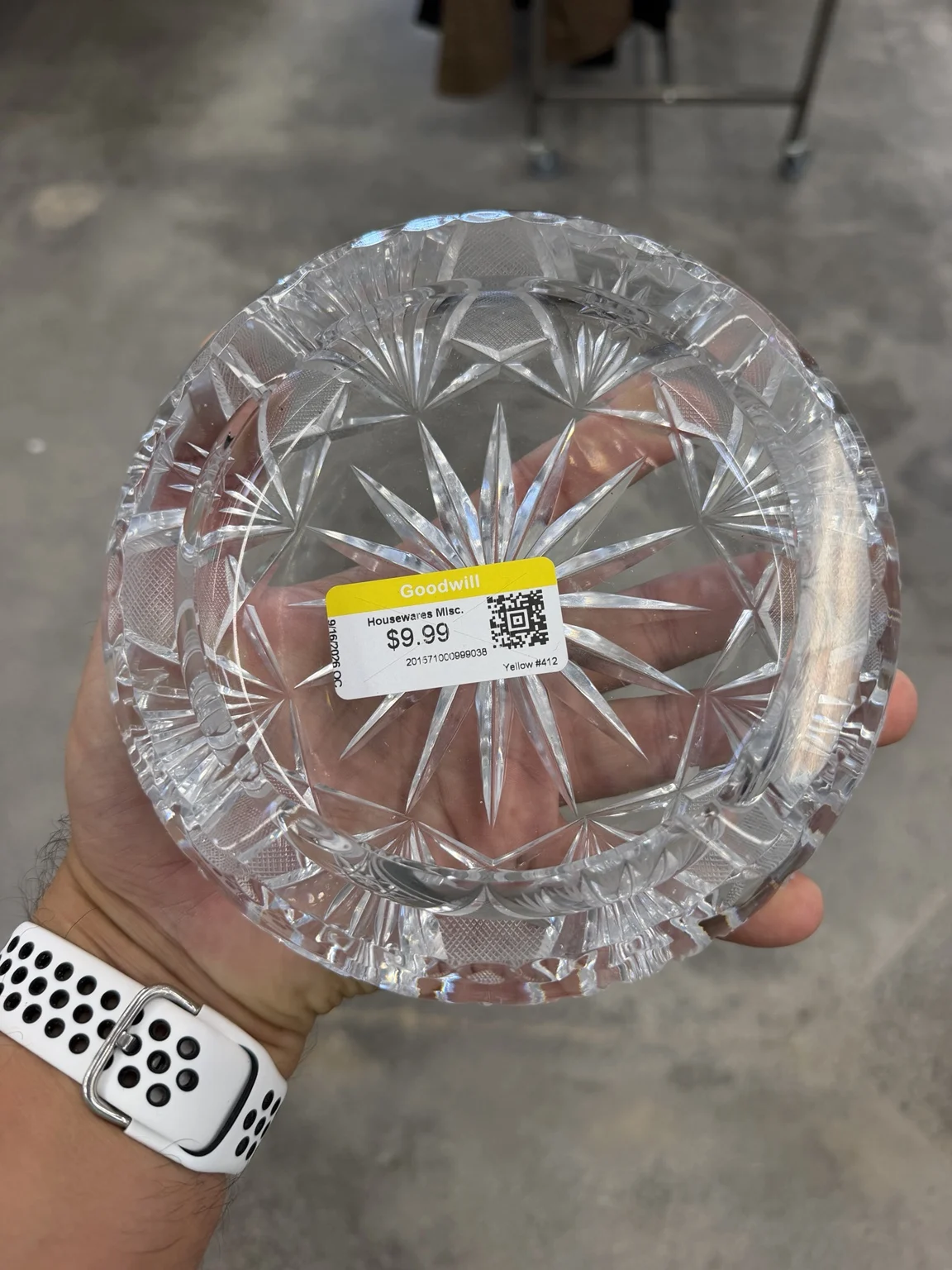 A large cut-glass or crystal-style ashtray held in one hand at Goodwill, with a $9.99 price sticker across its starburst center.
